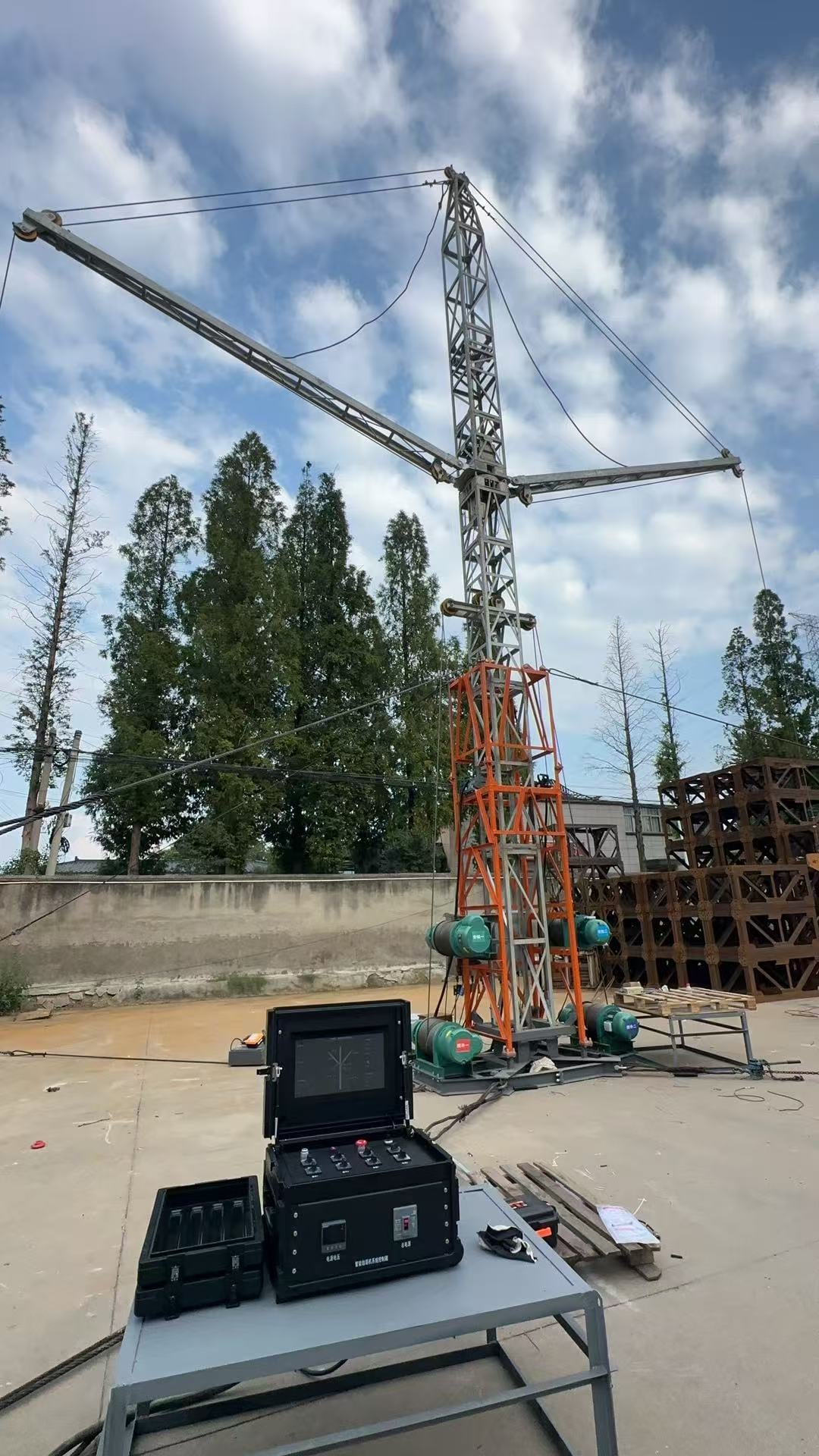 Full erection machine on site. The cage wraps the mast, the double jibs sit above, and the control box is in the foreground.
